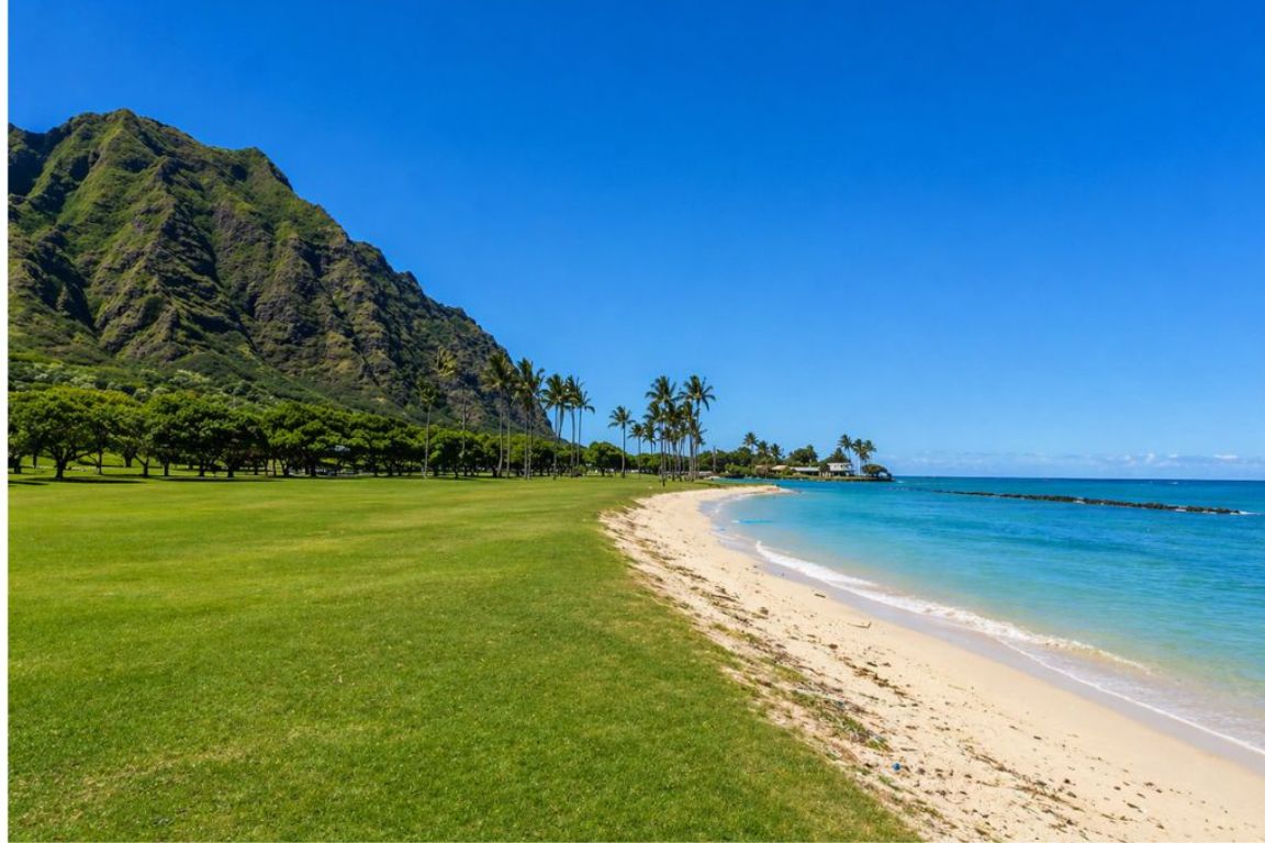 Kāneʻohe Bay shoreline with turquoise water, palm trees, and Koʻolau mountains during a Kualoa Ranch tour with our Kualoa Ranch Tours agency